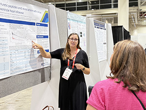 Elizabeth Thompson points to her poster while speaking with attendees at AHA25