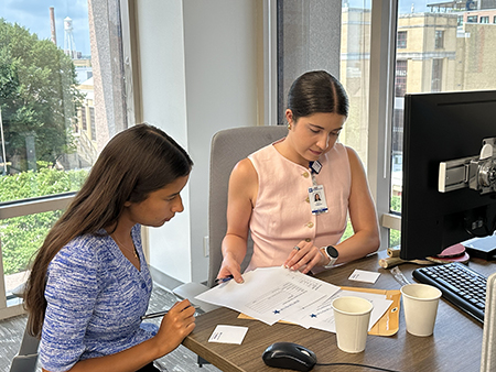 A STAR Program faculty member sits at a desk with a program attendee reviewing documents. They are seated in front of a window that overlooks Duke's campus.