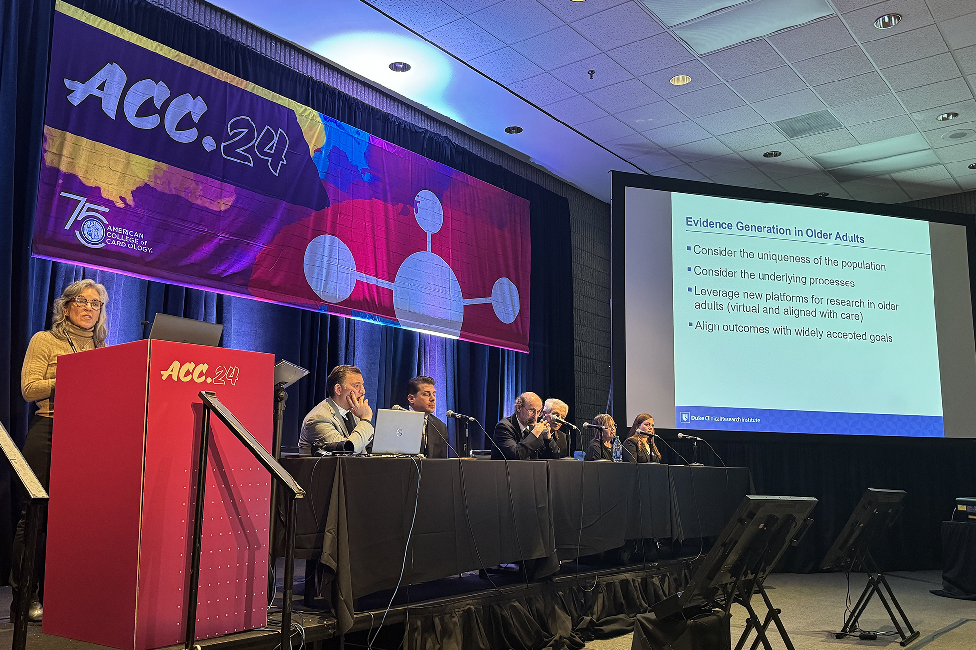 DCRI's Karen Alexander stands behind a podium presenting in front of a group of panelists. 