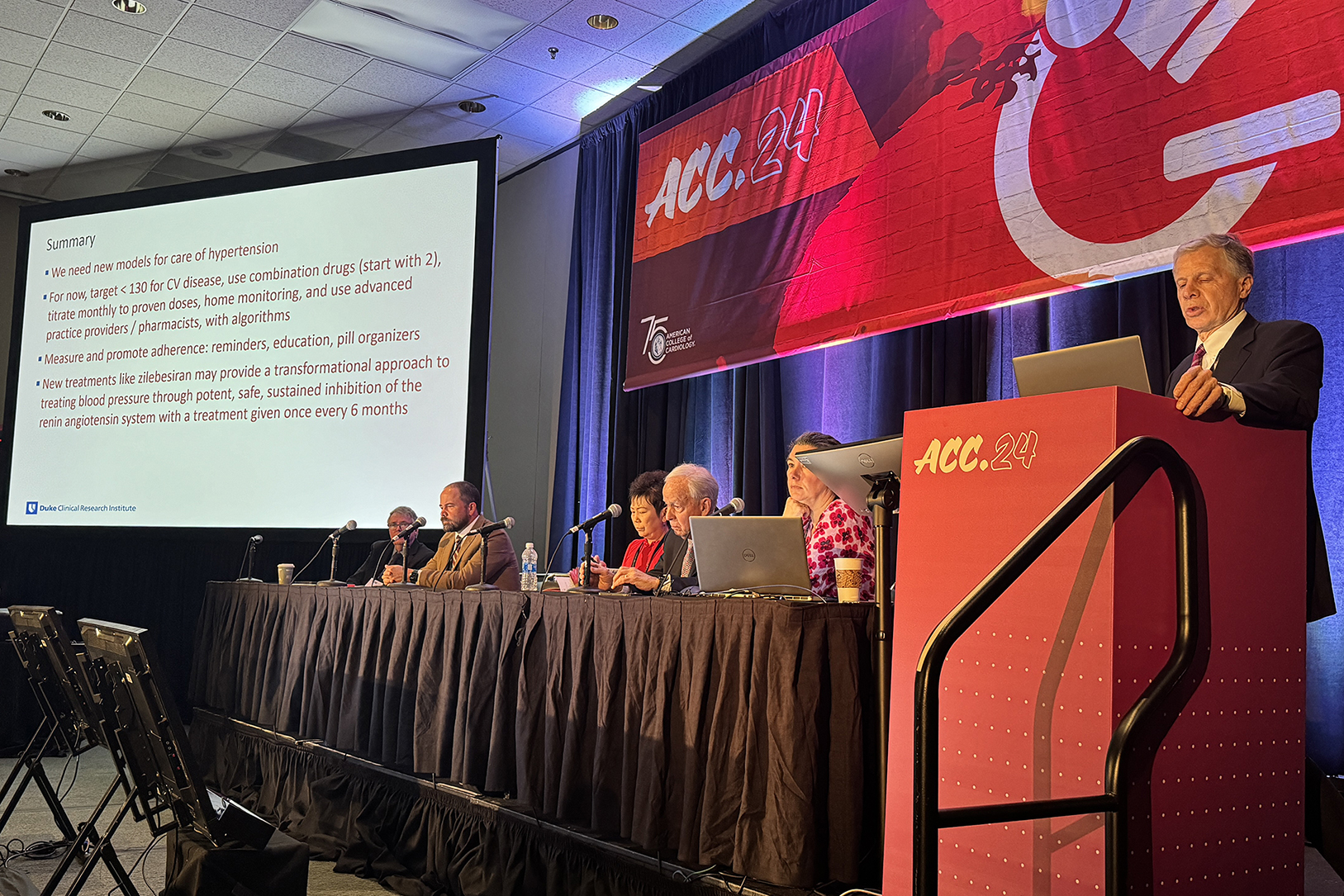 DCRI's Chris Granger stands behind a podium presenting a summary slide. 