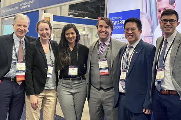 Five DCRI fellows stand together smiling at a conference alongside one of their DCRI faculty mentors.