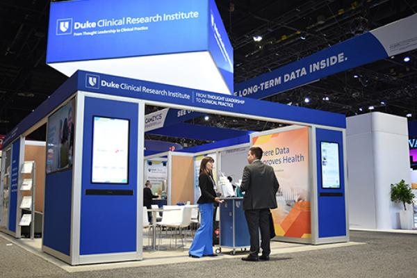 A wideshot of the DCRI exhibit booth at a recent conference. An operational expert stands at the entrance engaged in conversation with an attendee.