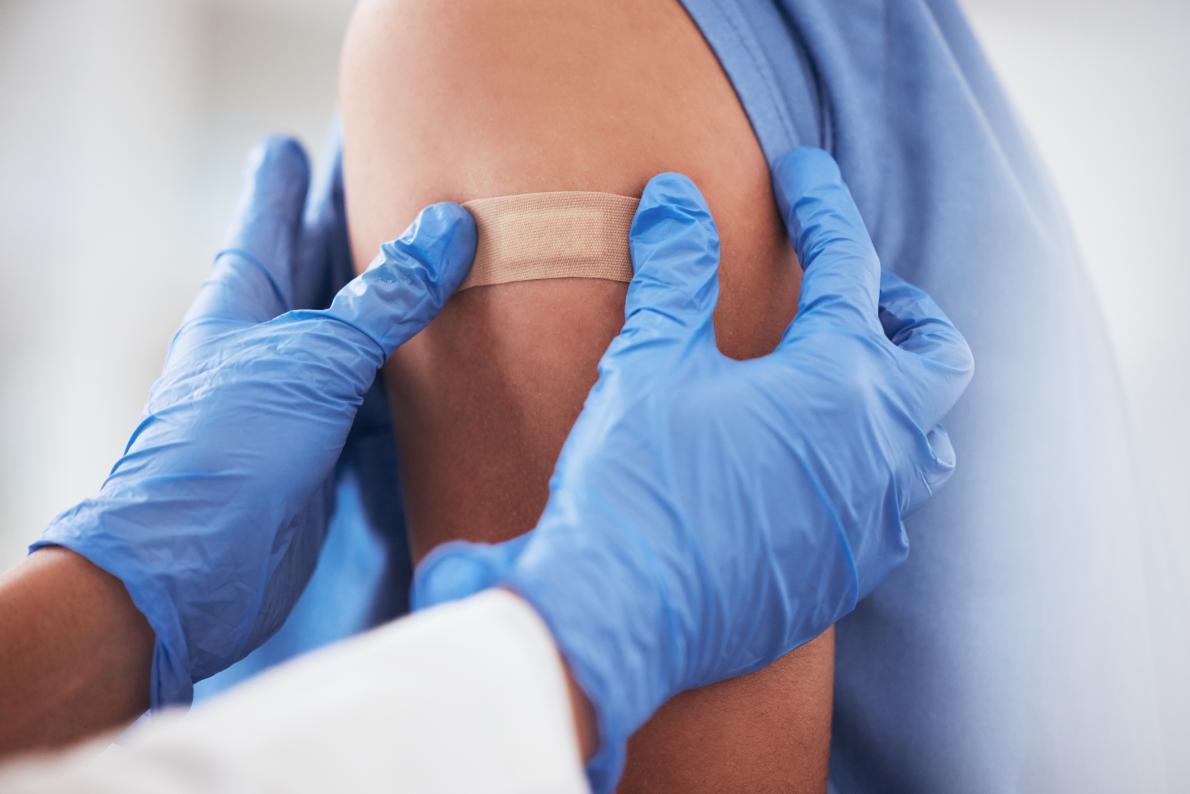 A clinician with gloves puts an adhesive bandage on a patient after administering a vaccination.